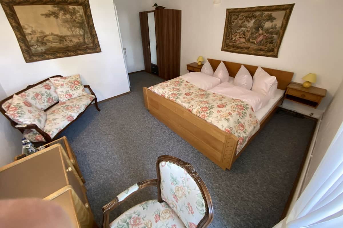 A bedroom with a bed, a chair, a wardrobe, and two paintings on the walls.