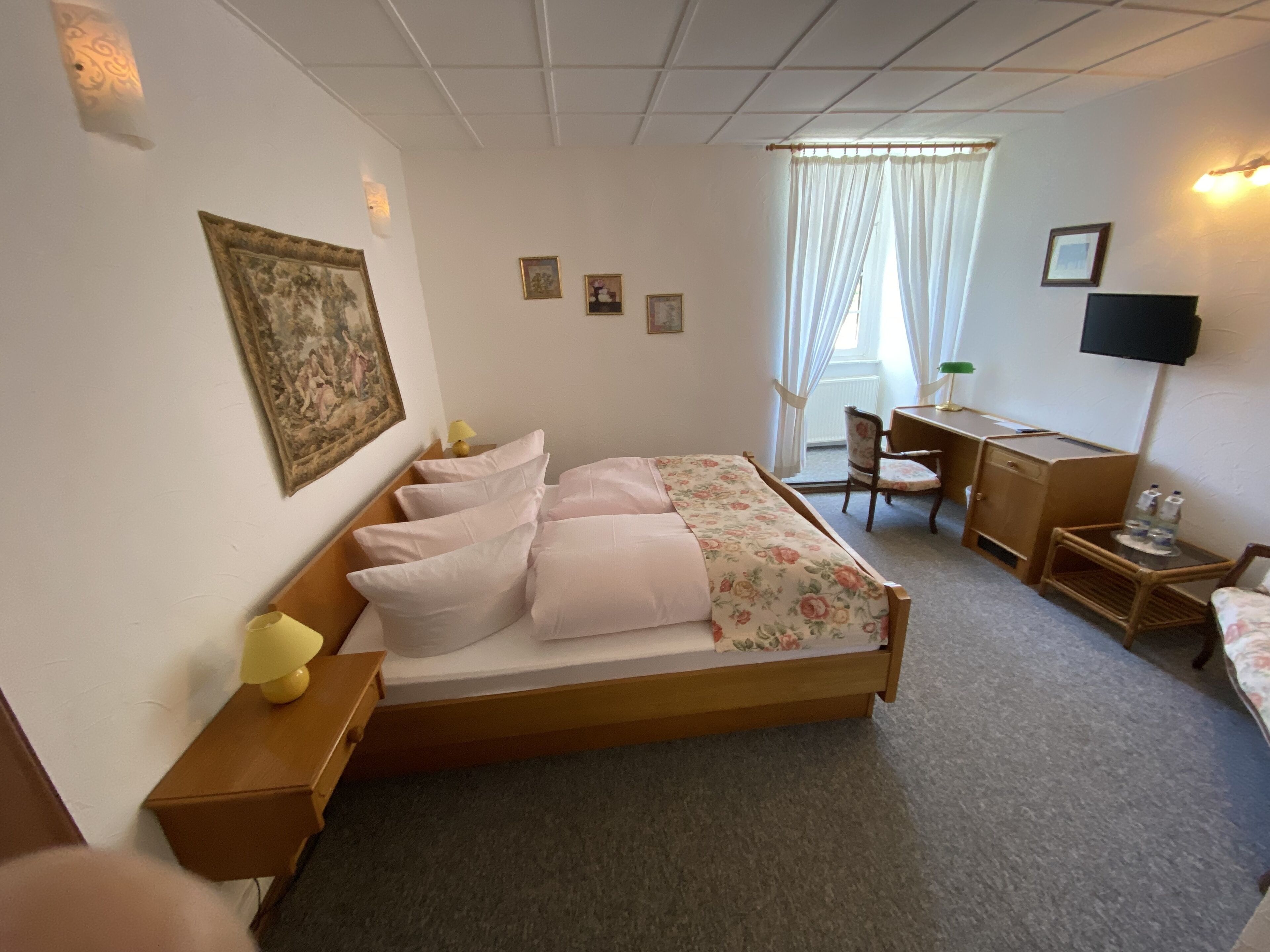 Hotelkamer met een enkel bed, een bureau, een stoel, een televisie en een raam met gordijnen.