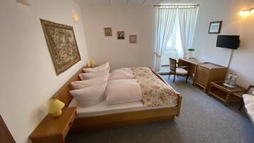 Une chambre d’hôtel avec un lit simple, un bureau, une chaise, une télévision et une fenêtre avec des rideaux.