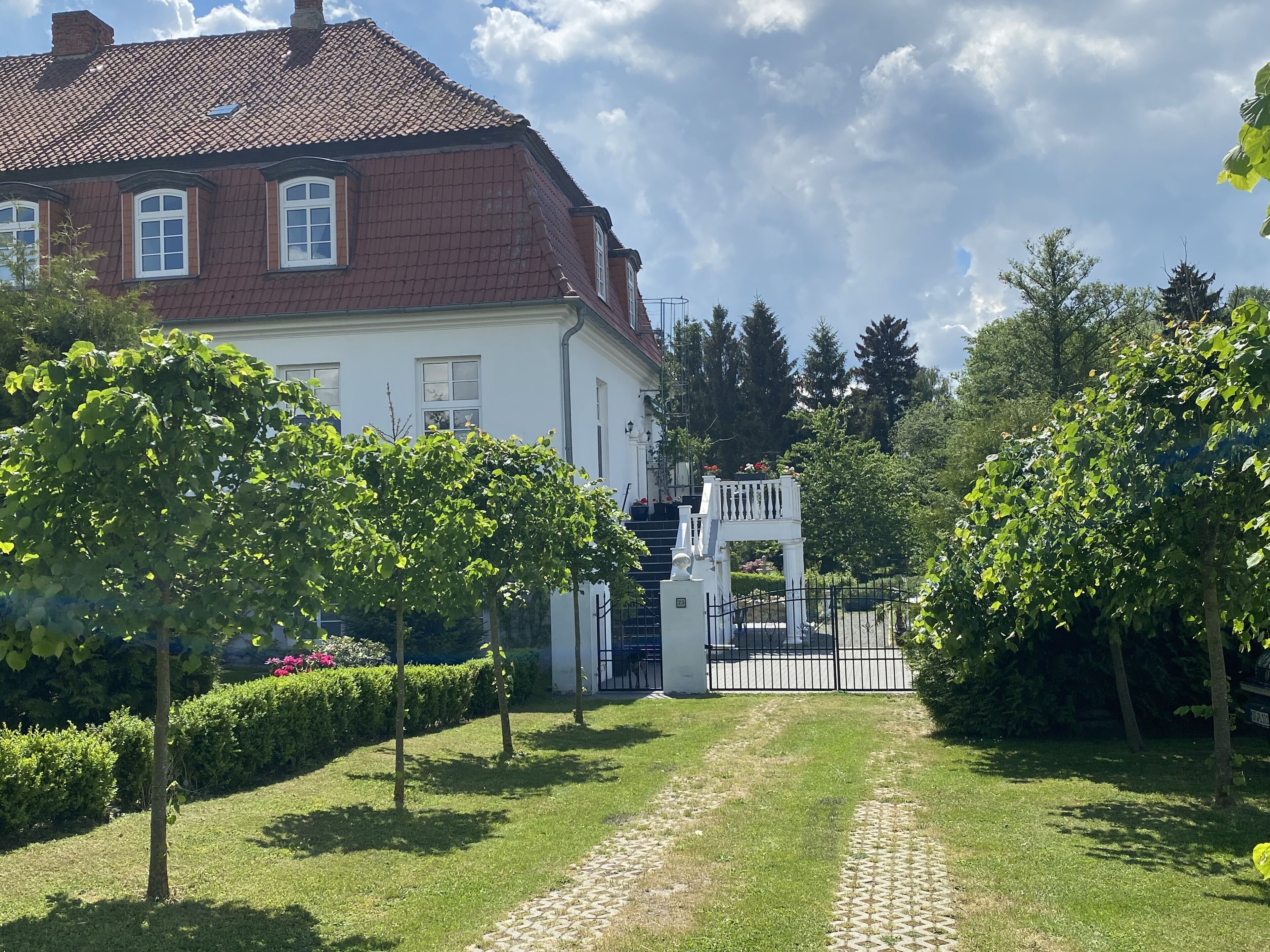 Ein Weg führt zu einem weißen Gebäude mit rotem Dach, umgeben von Grünflächen und einem verschlossenen Eingang.