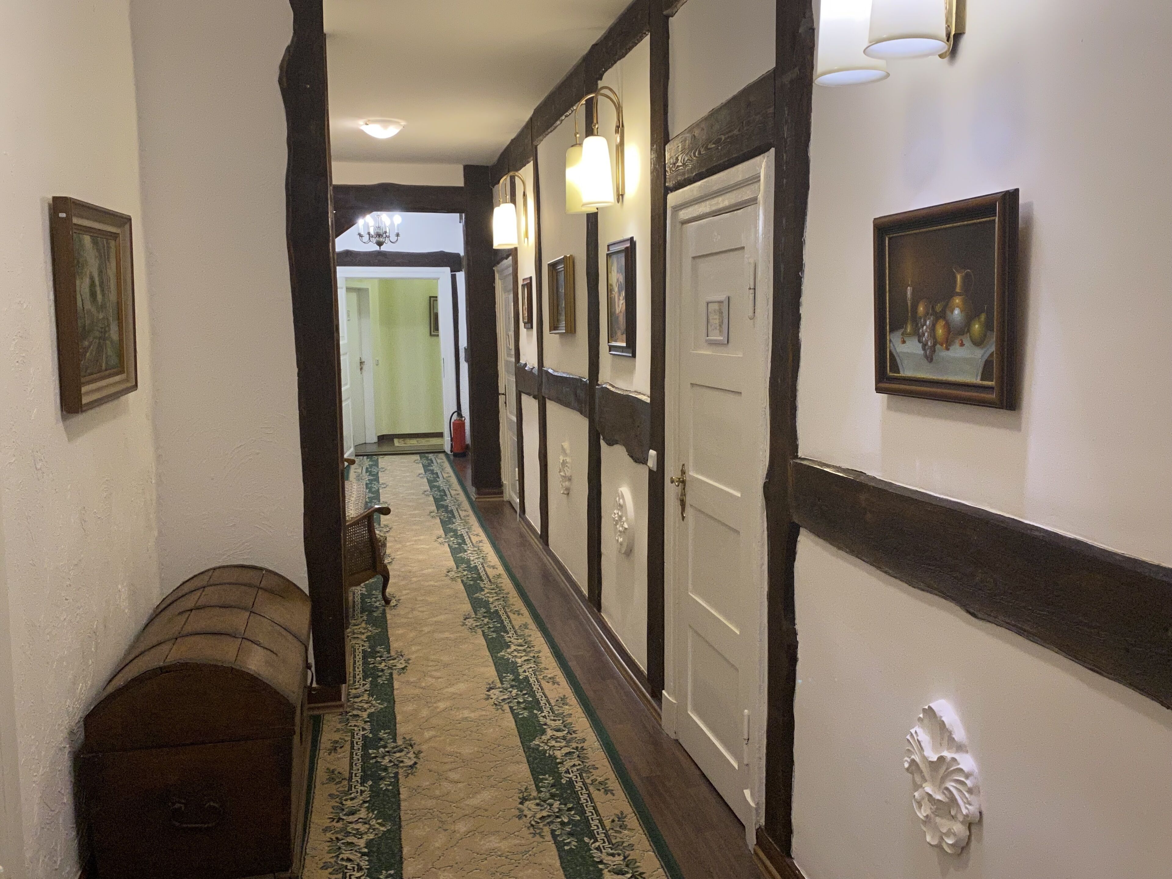 A hallway with a patterned carpet, wooden benches, and framed artwork on the walls.