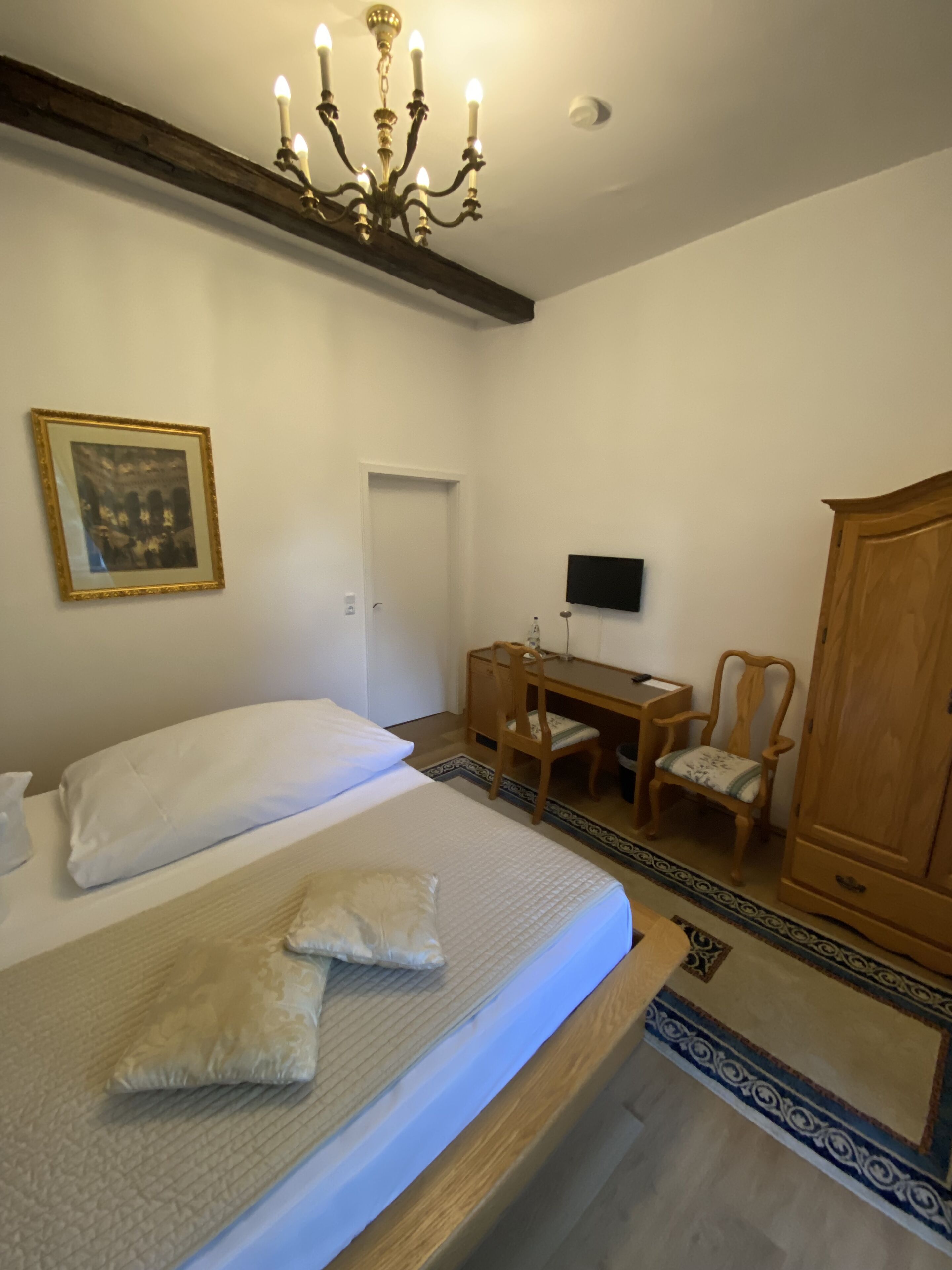 Quarto com cama, escrivaninha, cadeira, guarda-roupa, candelabro e um quadro na parede.