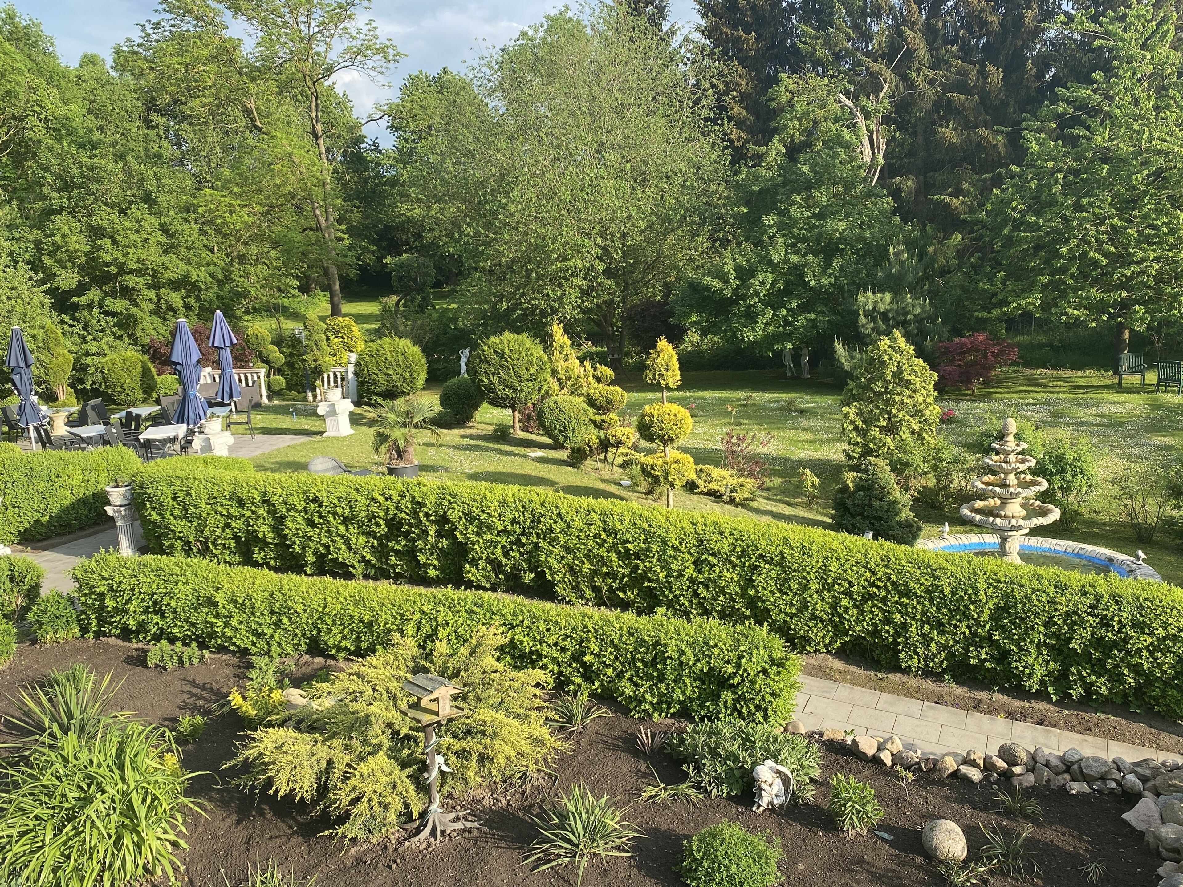 A well-maintained garden with neatly trimmed hedges, a central fountain, and outdoor seating areas.