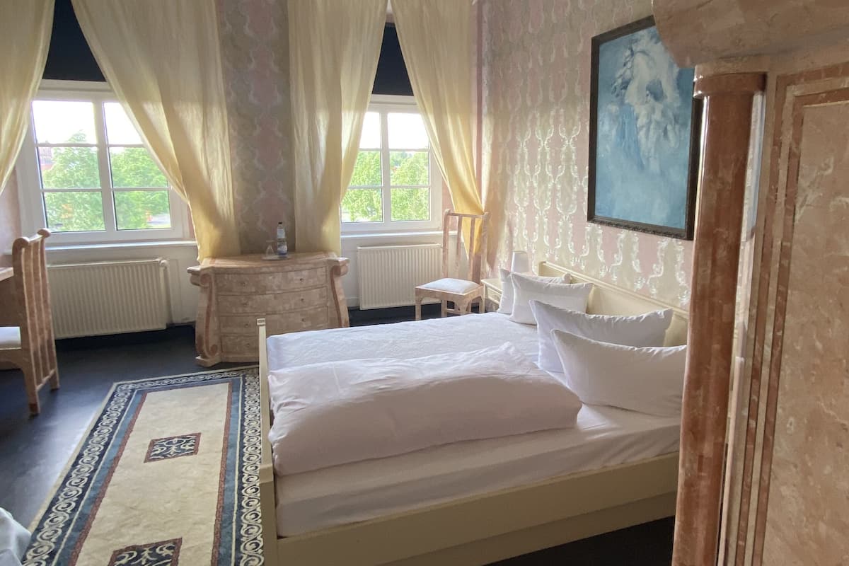 A bedroom with a large bed, a dresser, a chair, and a window with curtains.
