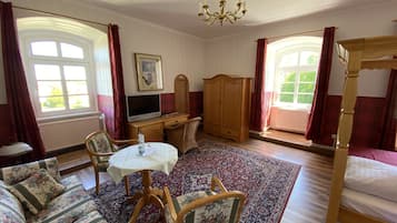 Una habitación con cama, escritorio con computadora, sofá, sillón, mesa y candelabro.