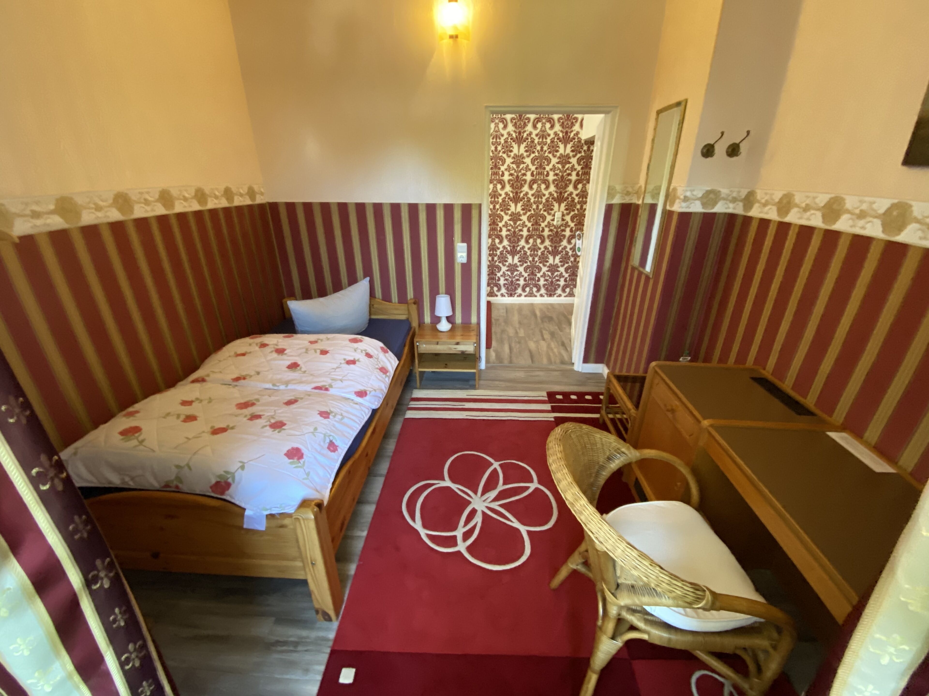 A bedroom with a single bed, a wooden nightstand, a chair, a dresser, and a small table with a lamp.