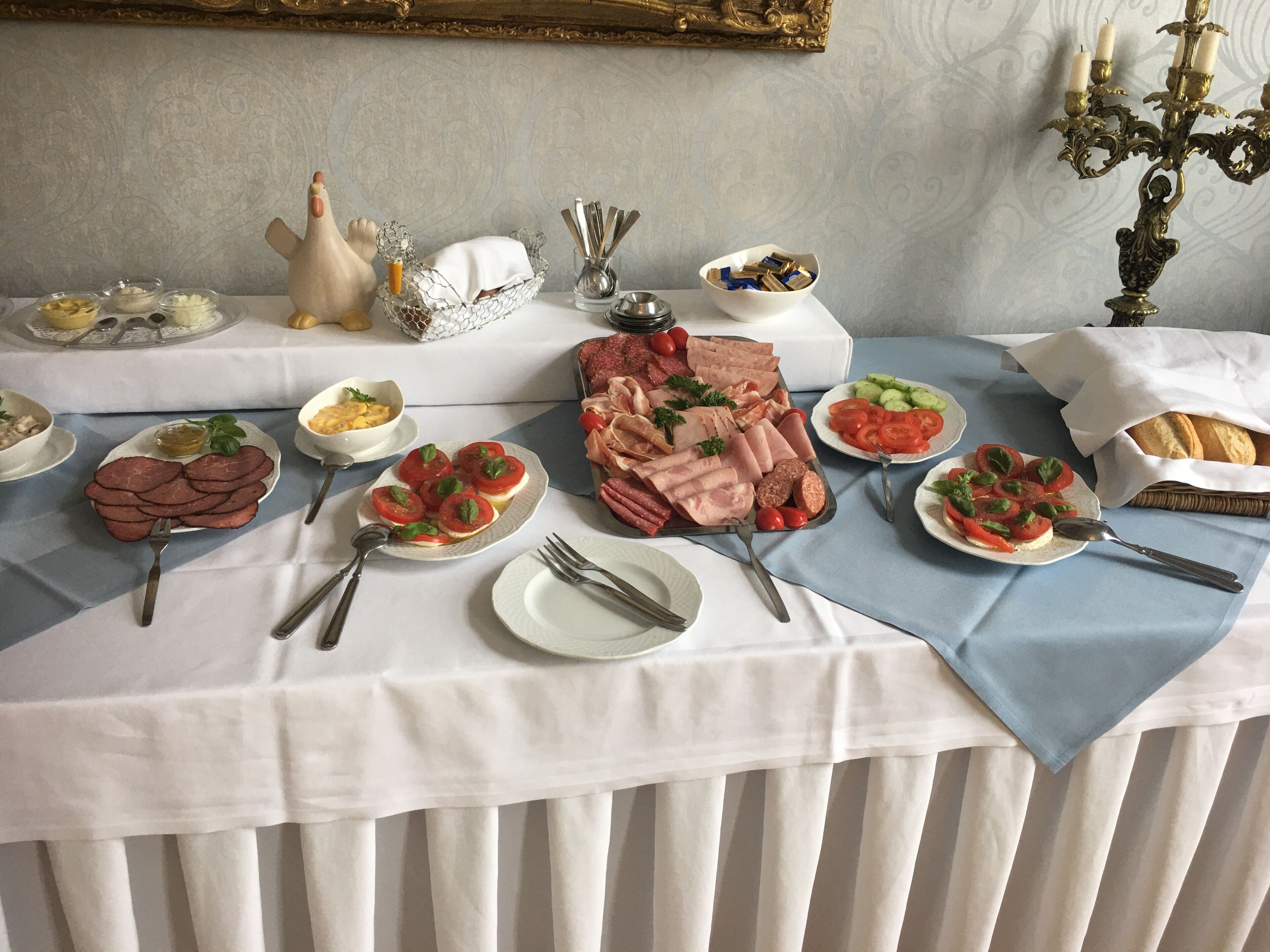 A table set with various dishes including meats, salads, and bread, with a decorative candelabra and a gold-framed mirror in the background.