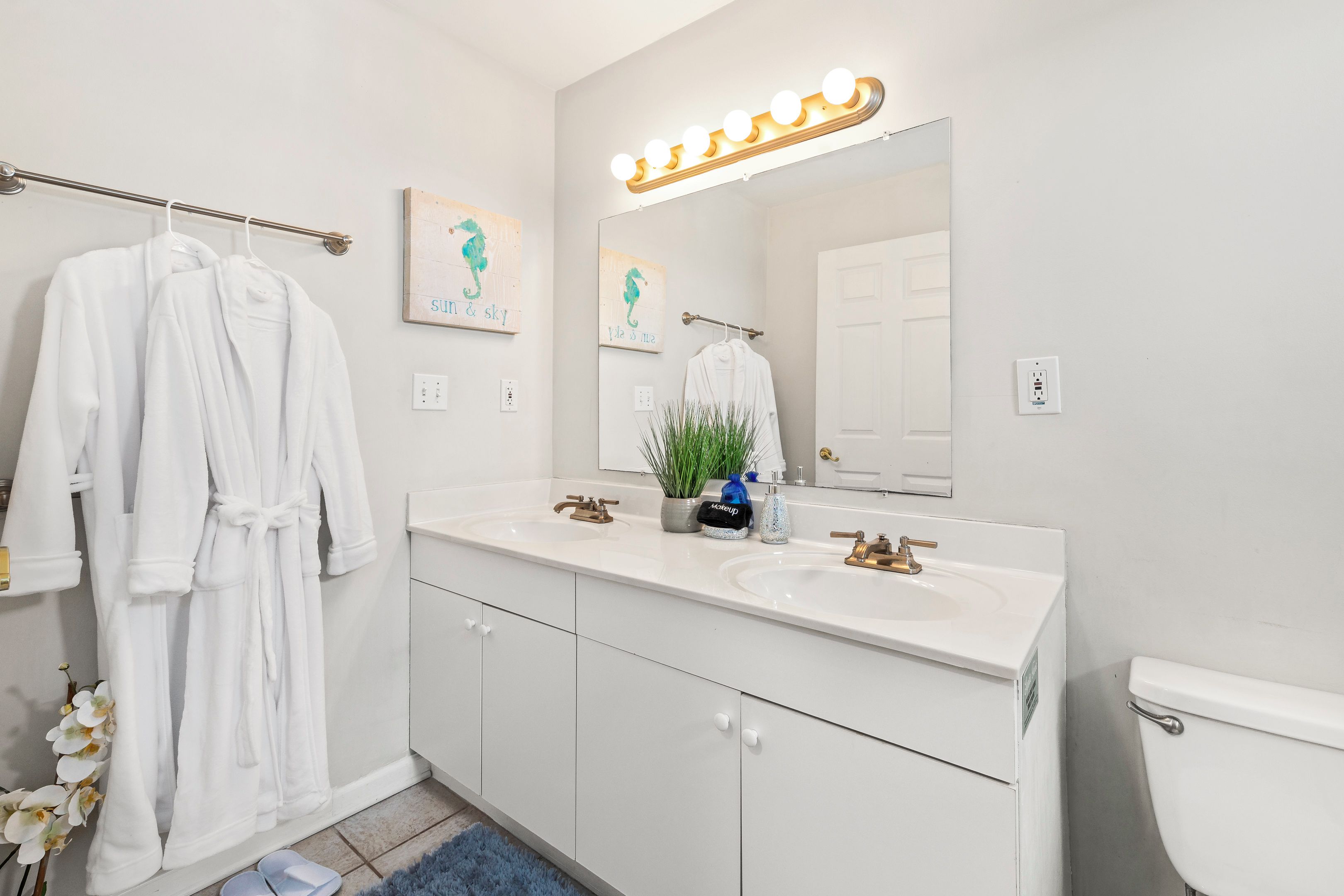 A bathroom with a white vanity, a mirror with lights, a towel rack, a toilet, and a sink with a faucet.