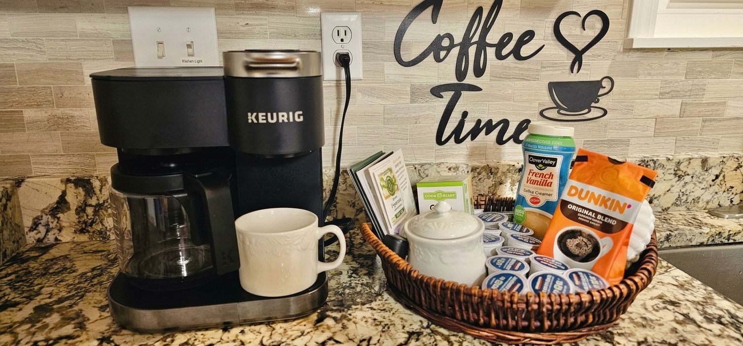 Una cafetera, una taza y una cesta con productos de café sobre una encimera de cocina.