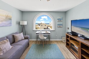 Ein Wohnzimmer mit Blick auf den Strand, einem Schreibtisch, einem Sofa und einem Fernseher.