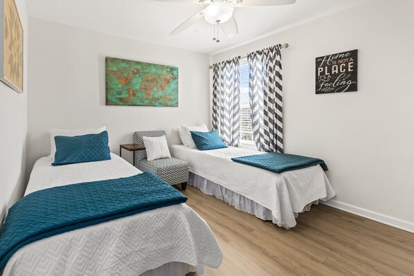 A bedroom with two beds, a ceiling fan, a world map, and a motivational quote on the wall.