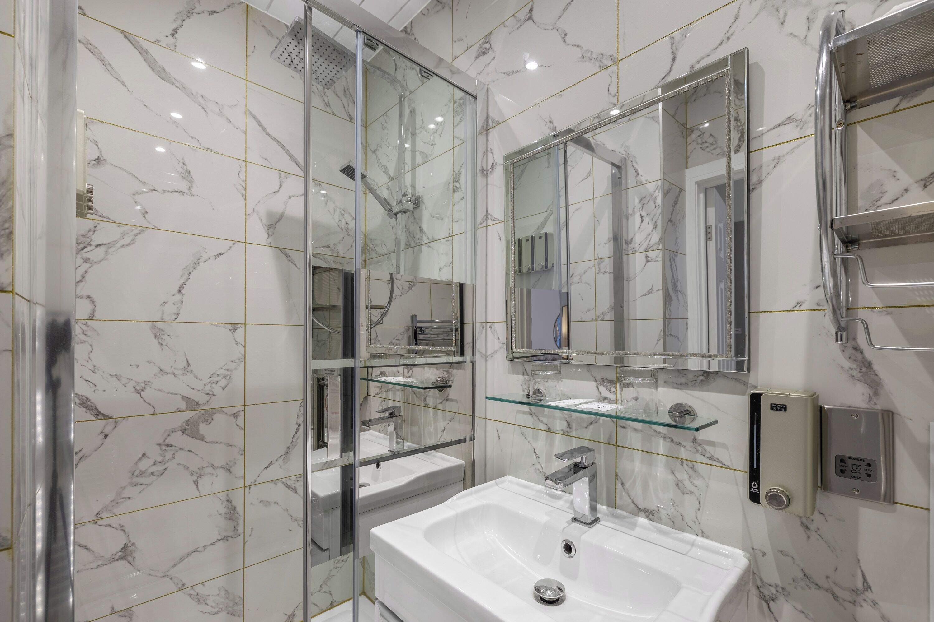 Un baño moderno con cabina de ducha de vidrio, un lavabo blanco con un solo grifo y un espejo grande sobre el lavabo.