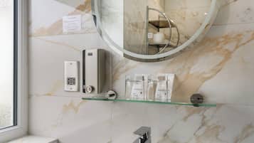 A bathroom with a marble wall, a glass shelf with shower caddies, a round mirror, and a modern faucet.