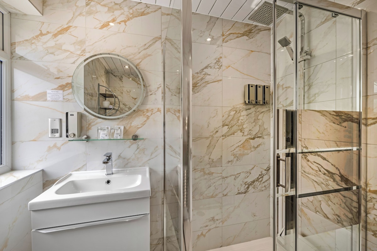 Un baño con pared de mármol, un lavamanos, un espejo y cabina de ducha de vidrio.