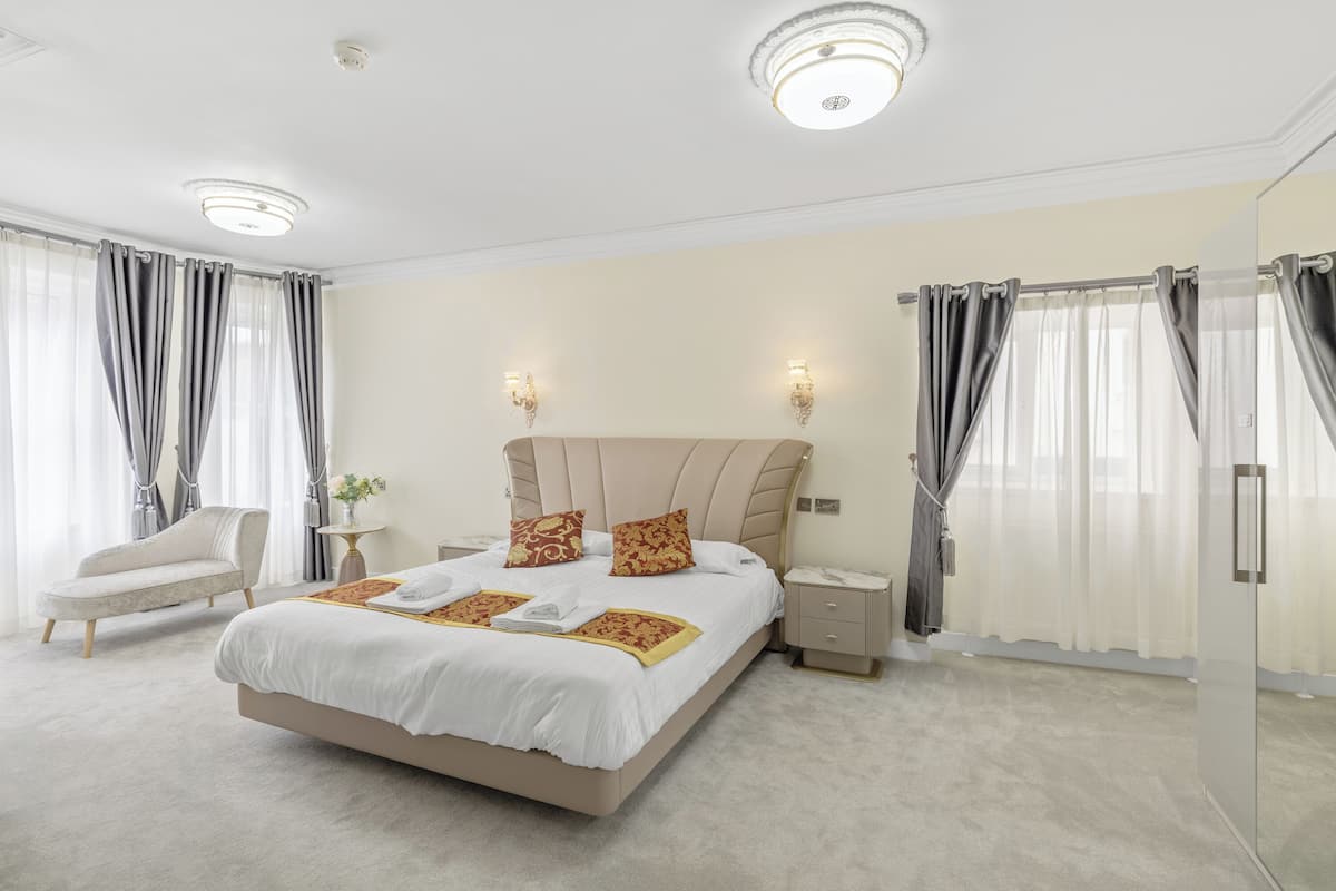 Une chambre spacieuse avec un grand lit, des tables de chevet, une chaise et une armoire fermée par des portes en verre.