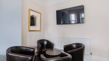 Een kamer met een grote flatscreen televisie aan de muur, een ronde tafel en drie leren stoelen.