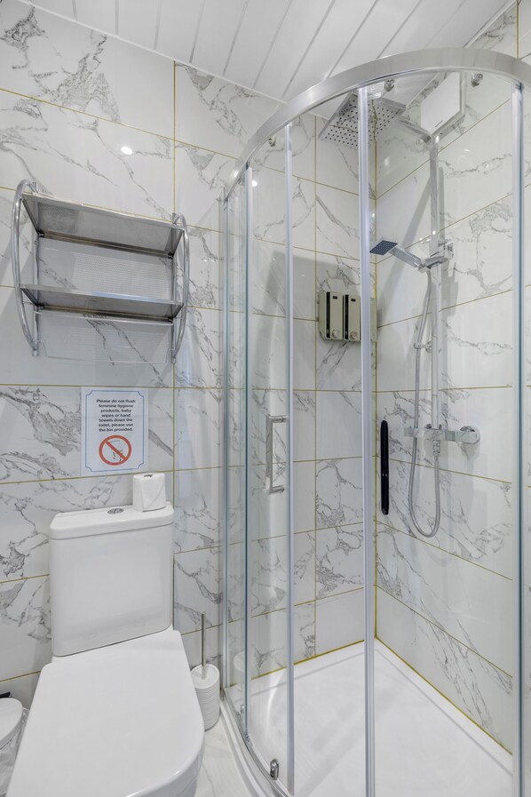 A modern bathroom with a glass-enclosed shower, a toilet, and a marble-patterned wall. - The Drake Hotel Plymouth (Plymouth)