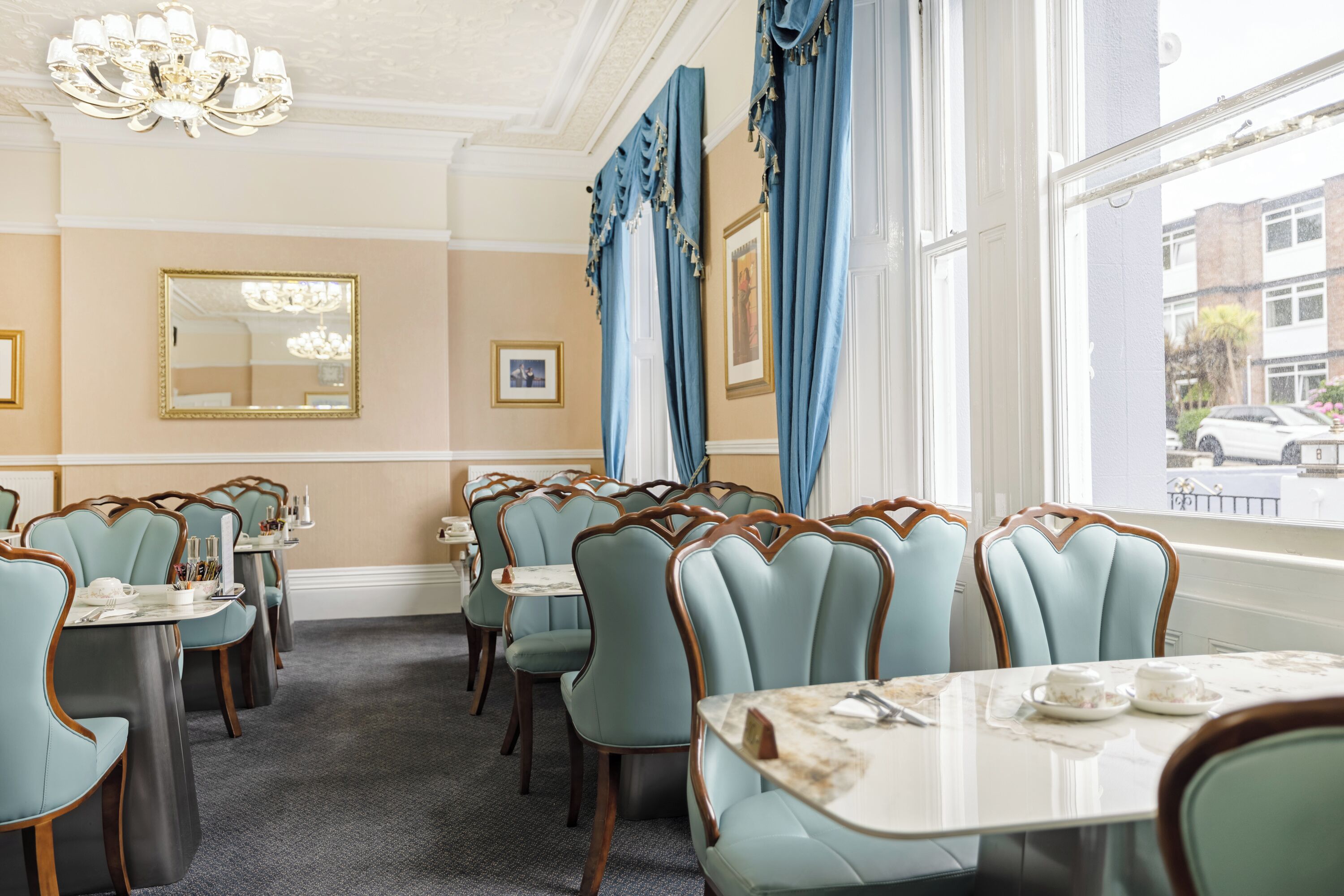 A dining area with light blue upholstered chairs, white marble tables, and blue curtains.