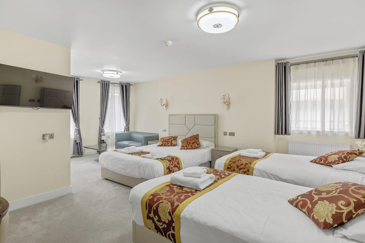 Une chambre d’hôtel avec trois lits, une télévision, un canapé et une grande fenêtre avec des rideaux.