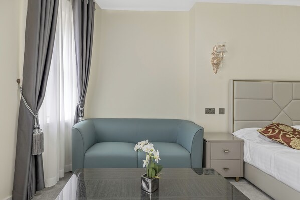 A modern hotel room with a blue sofa, a small table with a vase of flowers, a bedside table with a lamp, and a bed with patterned pillows. - The Drake Hotel Plymouth (Plymouth)