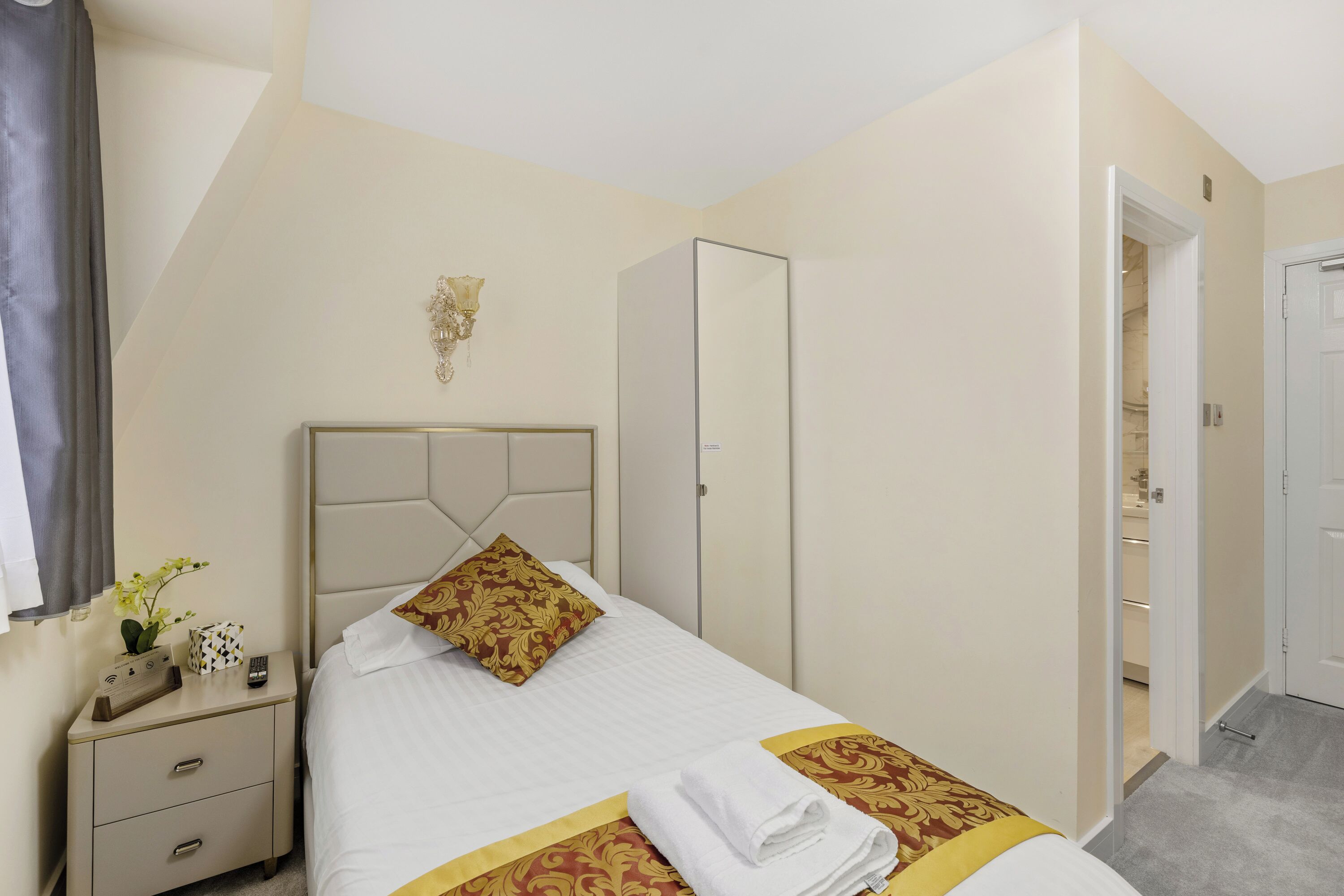 A neatly arranged hotel room with a bed, bedside table, and a wardrobe.