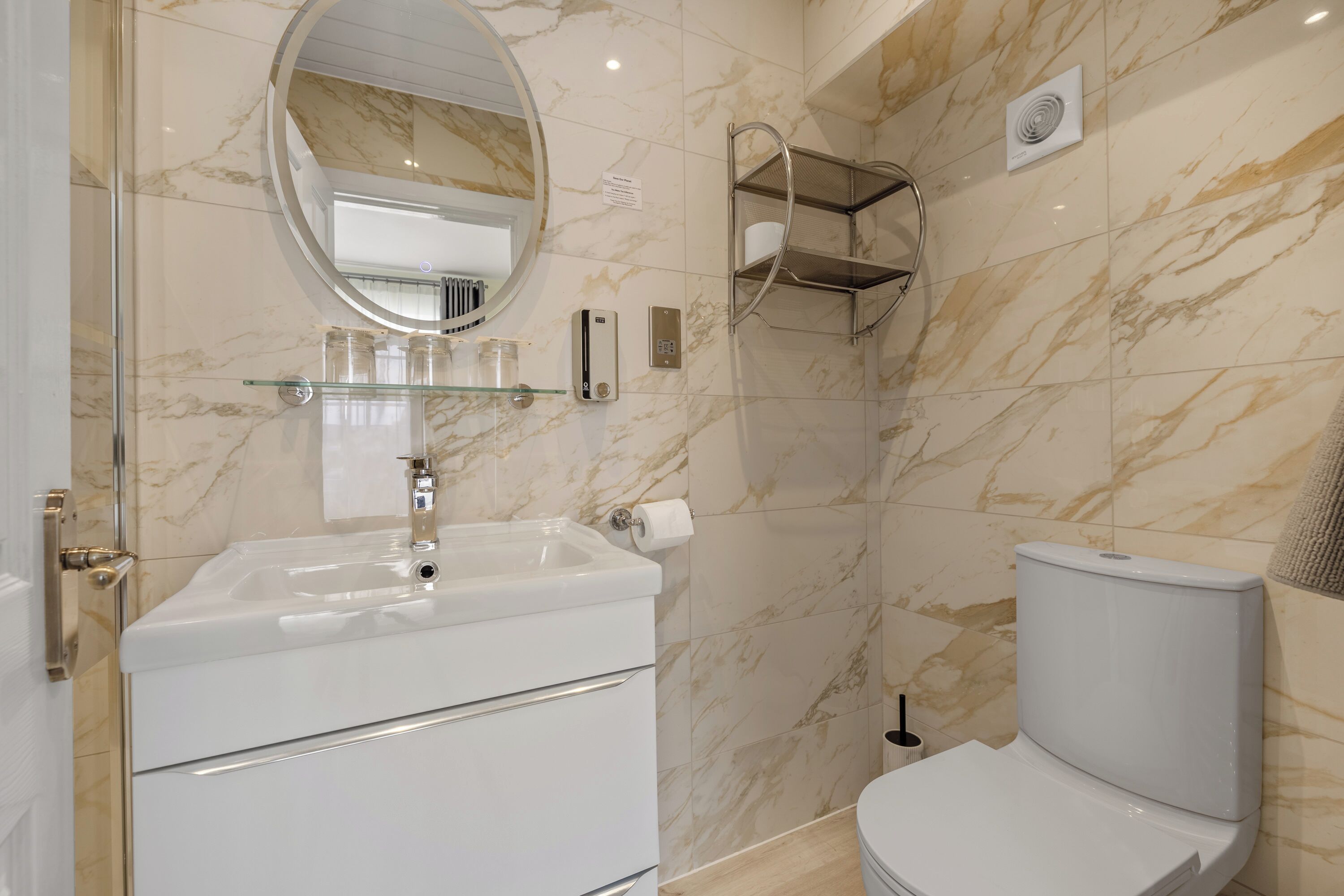 A bathroom with a white sink, a toilet, a glass shelf, a mirror, and a towel rack.
