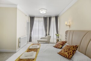 Habitación de hotel con una cama grande, una silla, una mesita con un florero y una lámpara fijada en la pared.