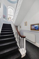 A staircase with white balusters and a wooden handrail, leading to a landing with a radiator and framed artwork.