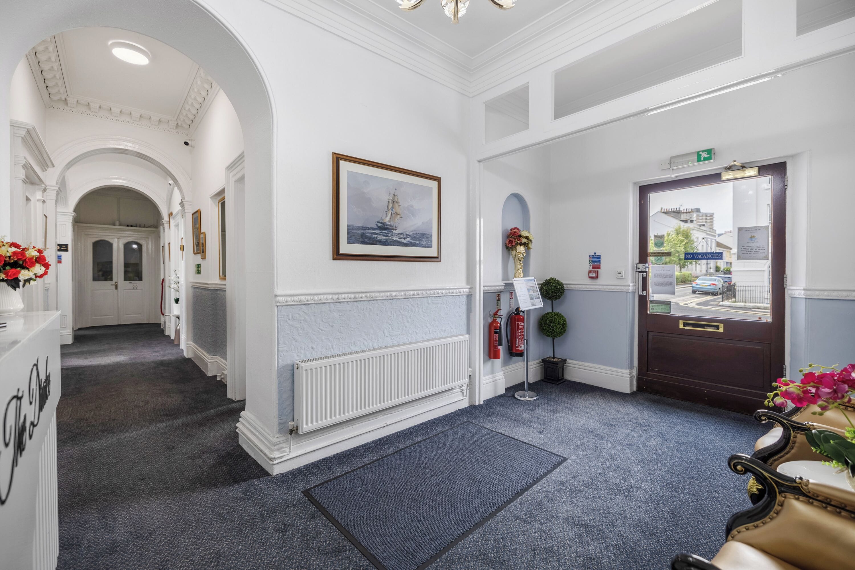 A hotel lobby with a grand entrance, a framed painting, a reception desk, and a fire extinguisher.