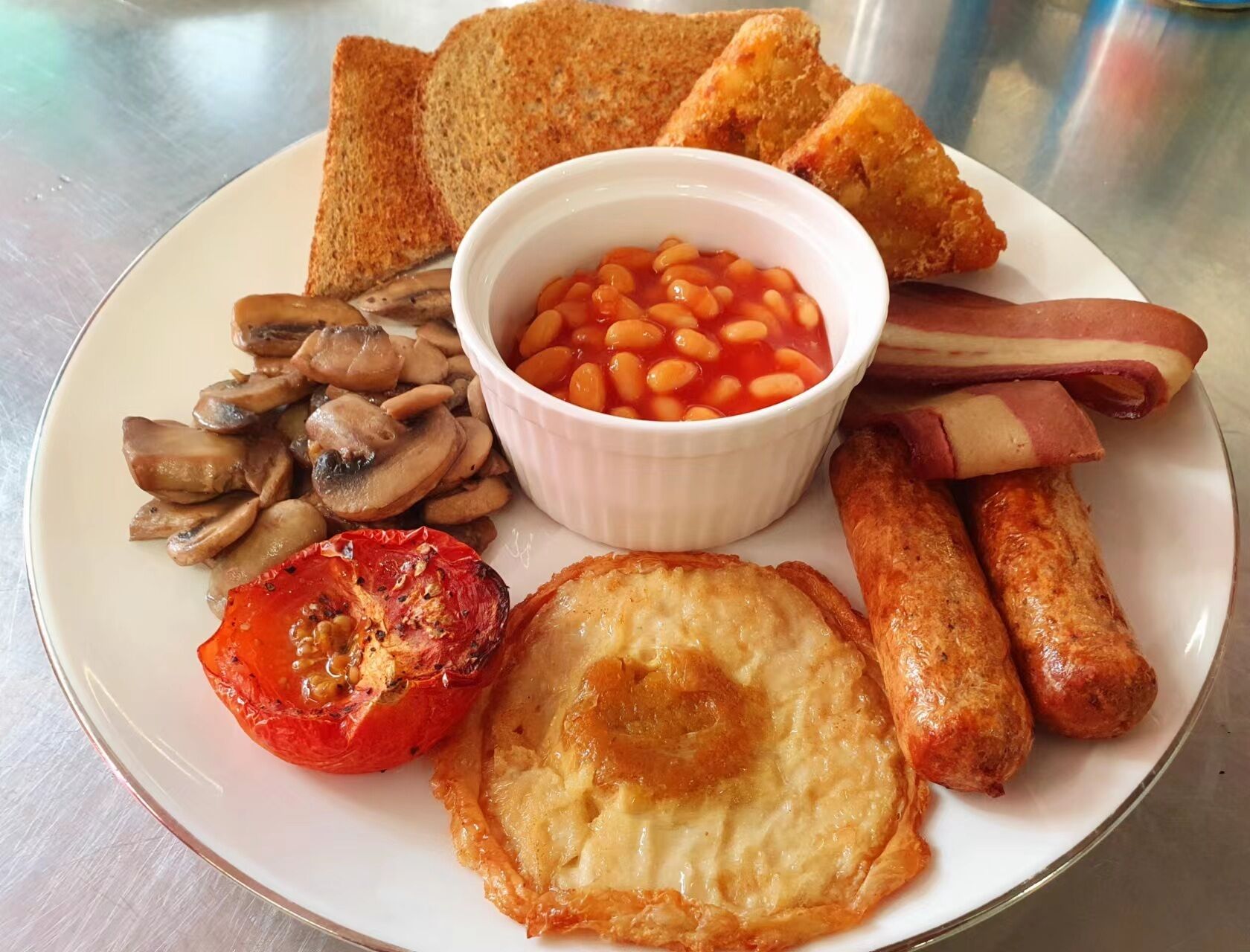A plate with toast, beans, bacon, mushrooms, a grilled tomato, and a fried egg.
