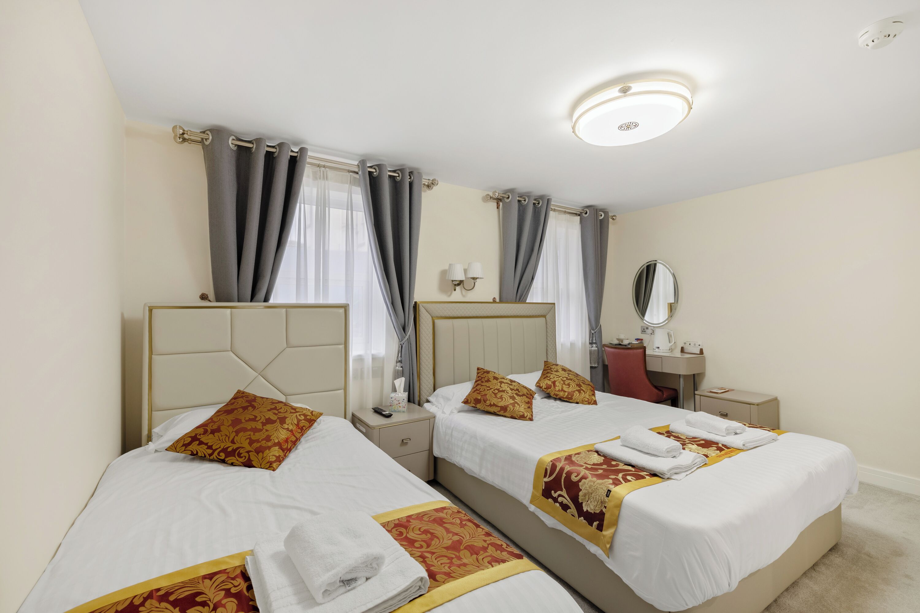 A hotel room with two beds, each with a headboard, a bedside table, a mirror, and a lamp.