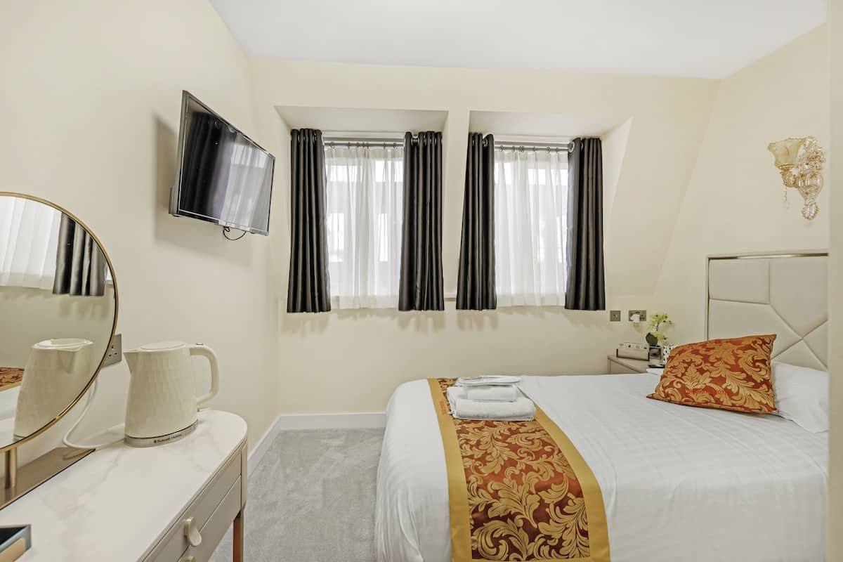 Une chambre d’hôtel avec un lit, un téléviseur fixé au mur, une table de chevet avec un vase et un miroir sur la commode.