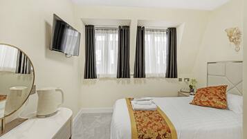 A hotel room with a bed, a TV mounted on the wall, a bedside table with a vase, and a mirror on the dresser.