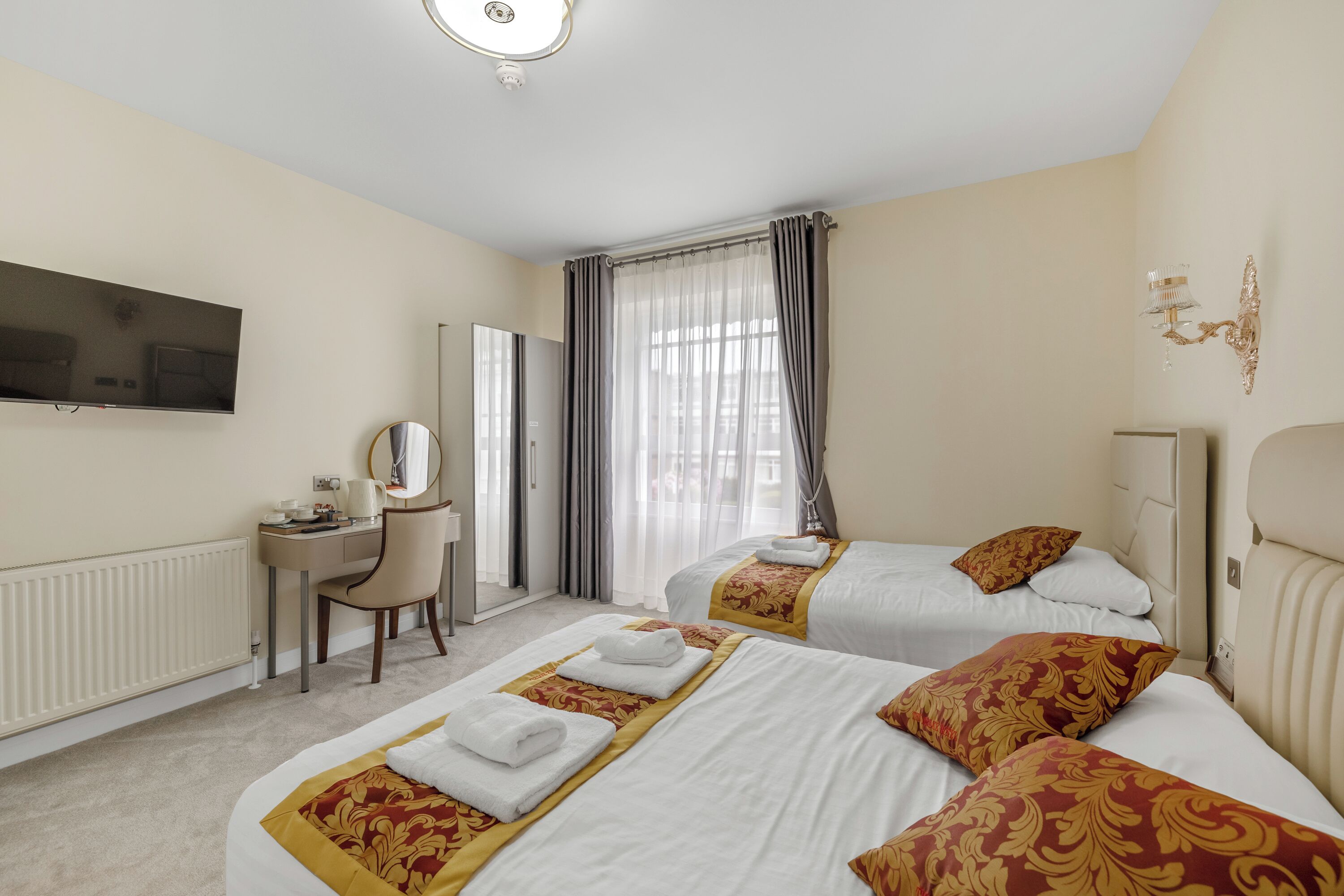 A hotel room with two beds, a desk, a television, and a window with curtains.