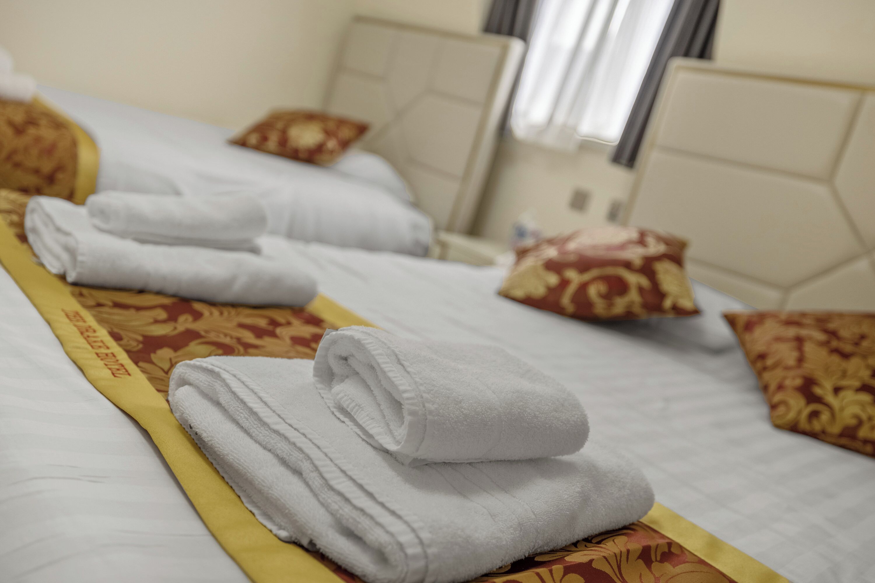 Habitación de hotel con toallas blancas ordenadas sobre las camas, una colcha estampada y cojines decorativos.