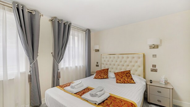 Une chambre d’hôtel avec un grand lit, deux oreillers, une table de chevet avec une lampe et une fenêtre avec des rideaux.