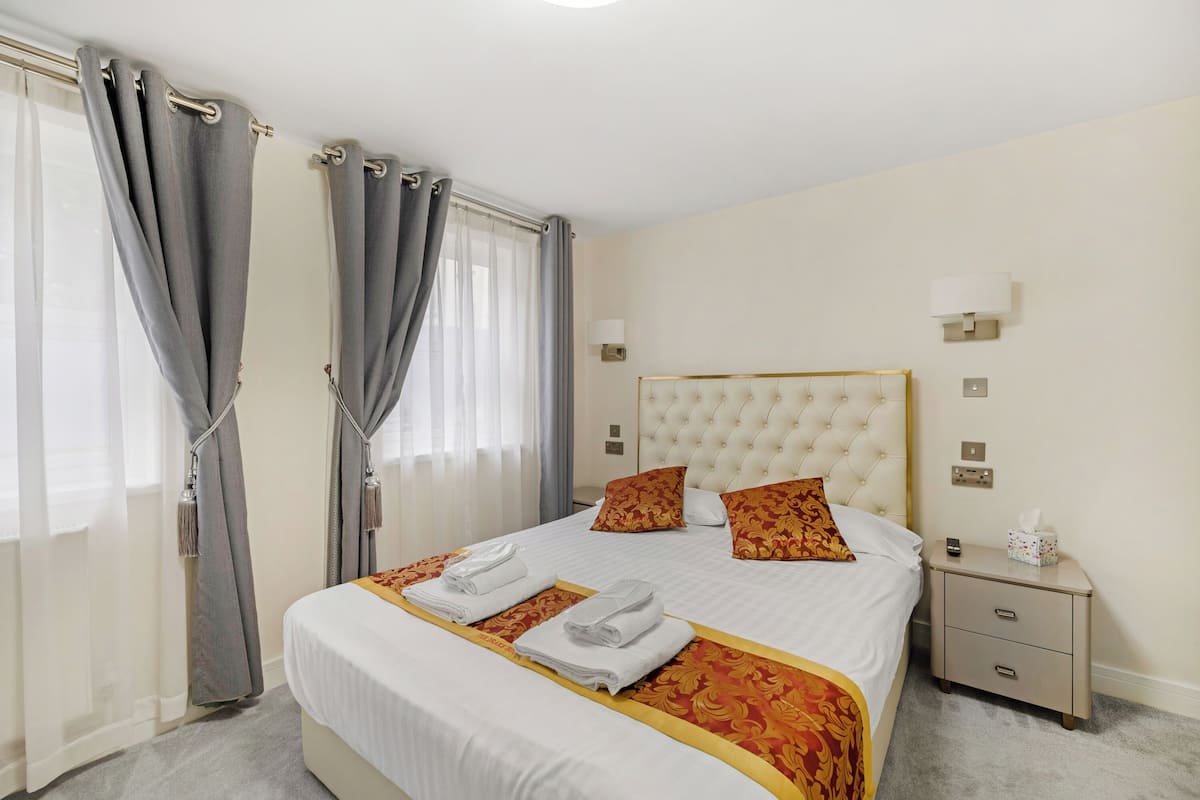 Une chambre d’hôtel avec un grand lit, deux oreillers, une table de chevet avec une lampe et une fenêtre avec des rideaux.