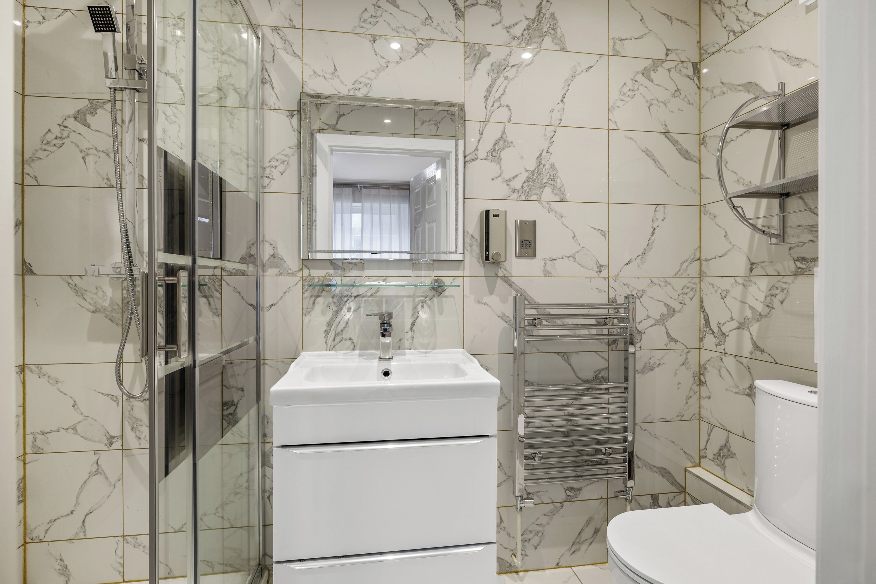 Un baño moderno con ducha de vidrio, lavamanos blanco, espejo e inodoro.