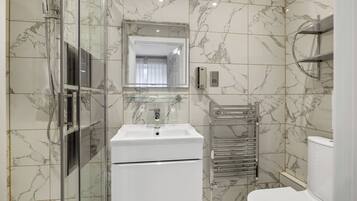 Un baño moderno con ducha de vidrio, lavamanos blanco, espejo e inodoro.