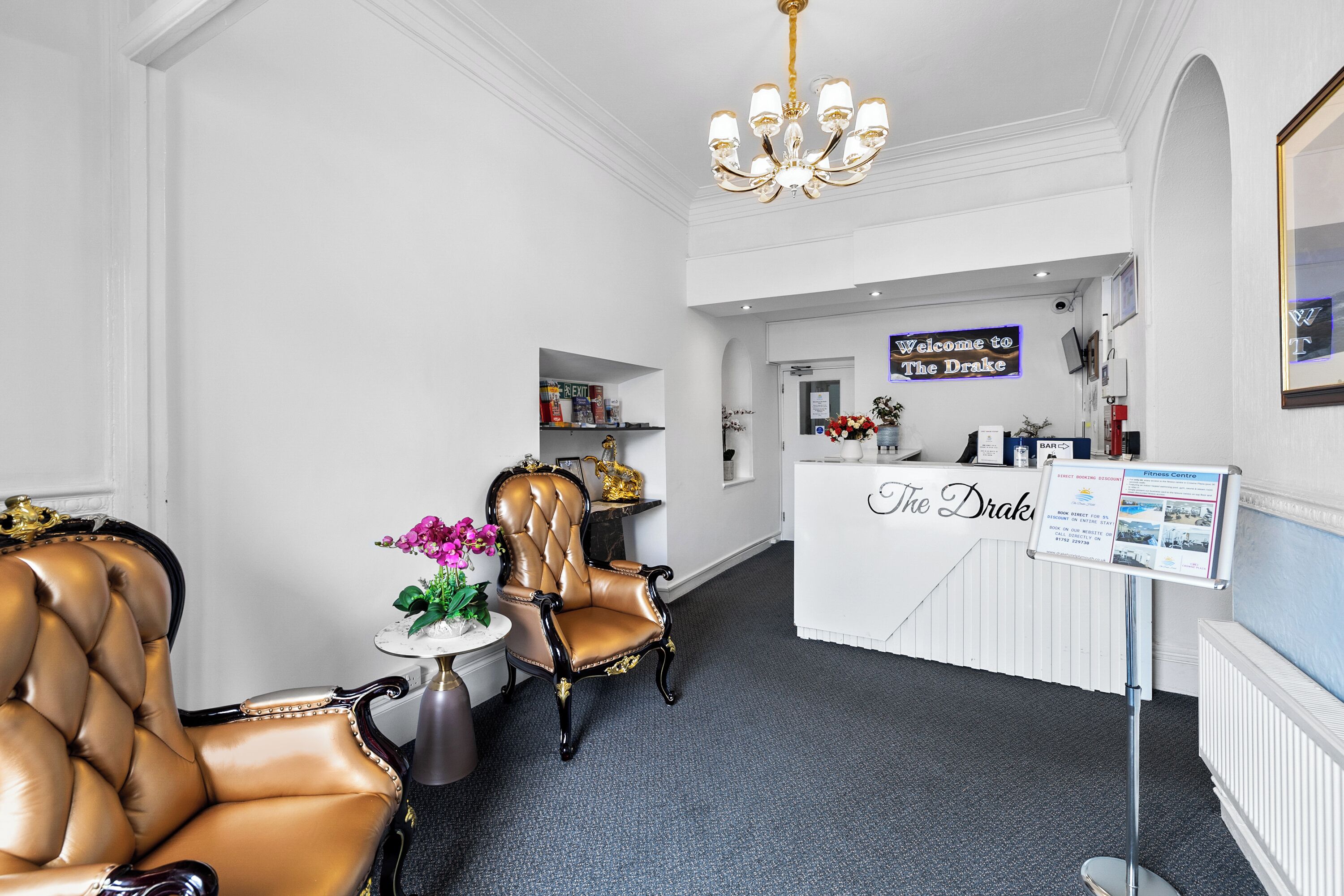 Un espace d’accueil comprenant un comptoir de réception, un lustre, un fauteuil en cuir et une petite table agrémentée de fleurs.