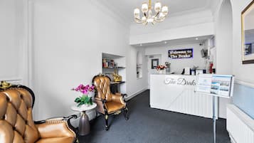 Un espace d’accueil comprenant un comptoir de réception, un lustre, un fauteuil en cuir et une petite table agrémentée de fleurs.