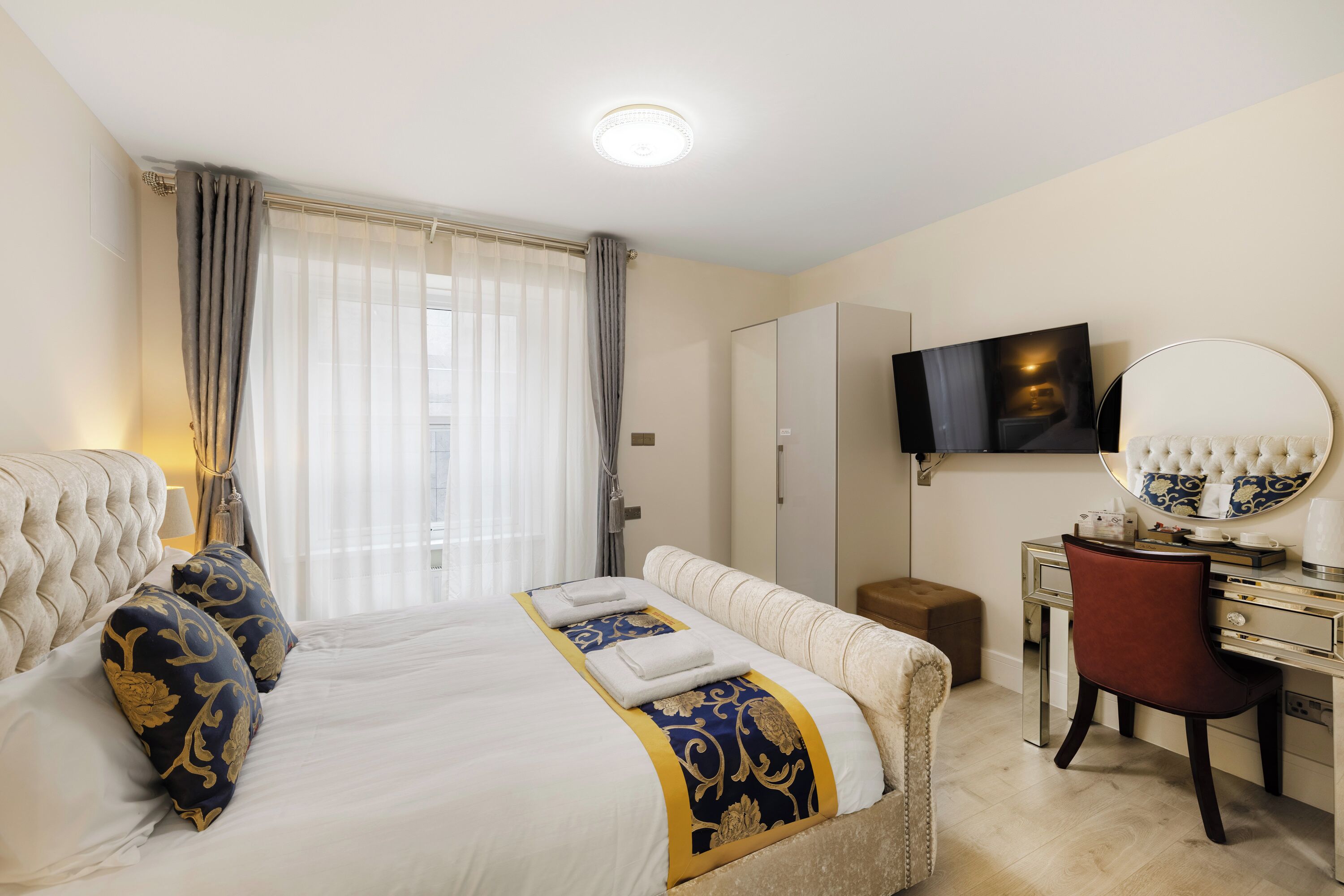 A hotel room with a large bed, a desk, a chair, a TV, and a mirror.