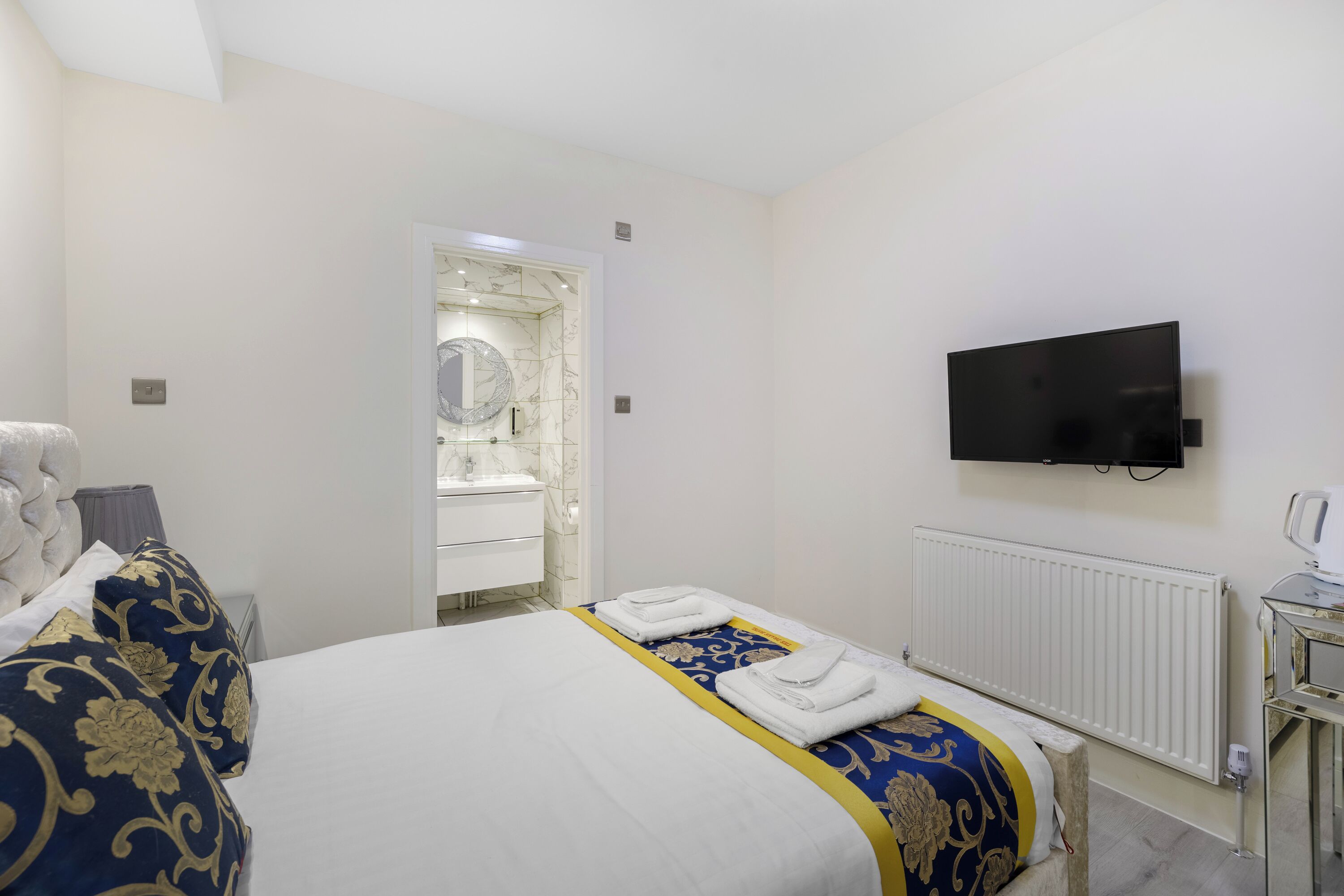 A hotel room with a bed, a television, a bathroom with a mirror, and a radiator.