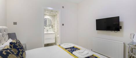 A hotel room with a bed, a television, a bathroom with a mirror, and a radiator.