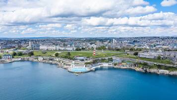 Vista aérea de una ciudad costera con un faro destacado, un puerto deportivo y una mezcla de edificios modernos e históricos.