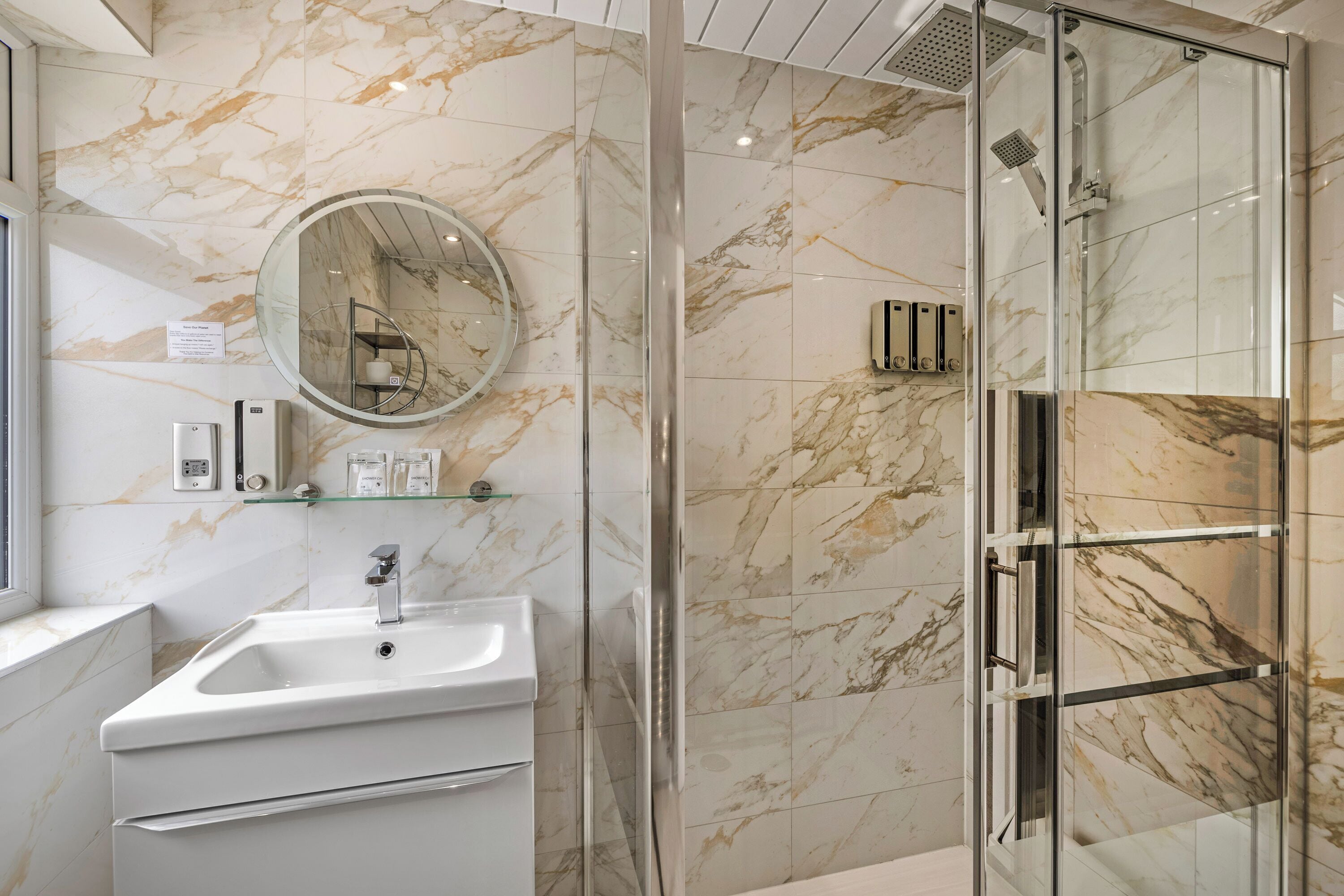 A bathroom with a marble wall, a sink, a mirror, and a glass shower enclosure.