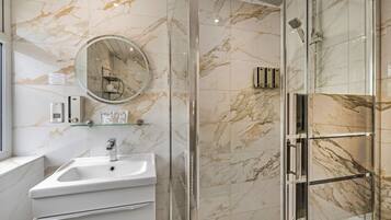 Un baño con pared de mármol, un lavamanos, un espejo y cabina de ducha de vidrio.