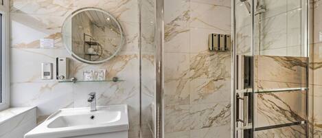 A bathroom with a marble wall, a sink, a mirror, and a glass shower enclosure.
