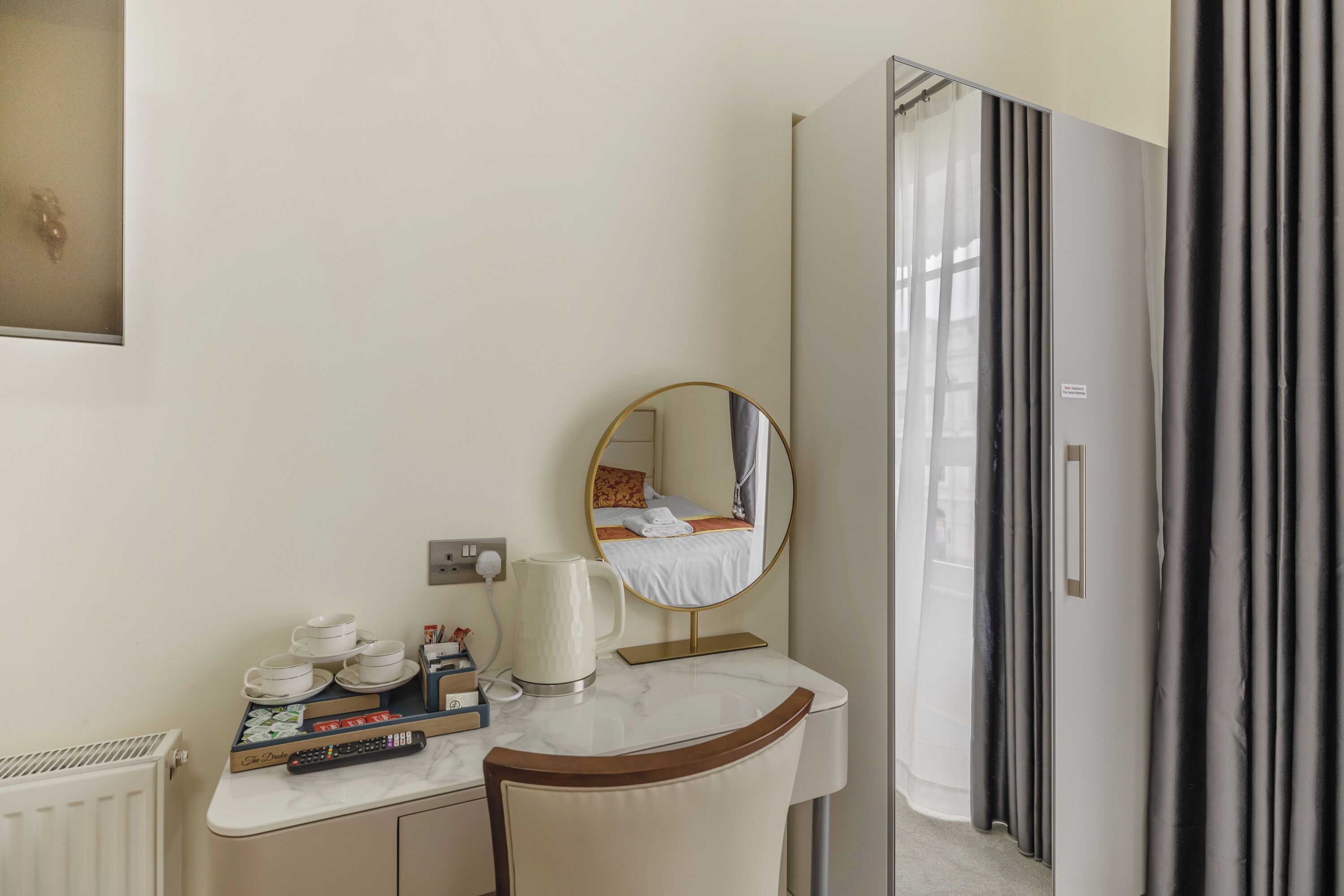 A hotel room with a marble desk, a mirror, a bed with curtains, and a wardrobe.