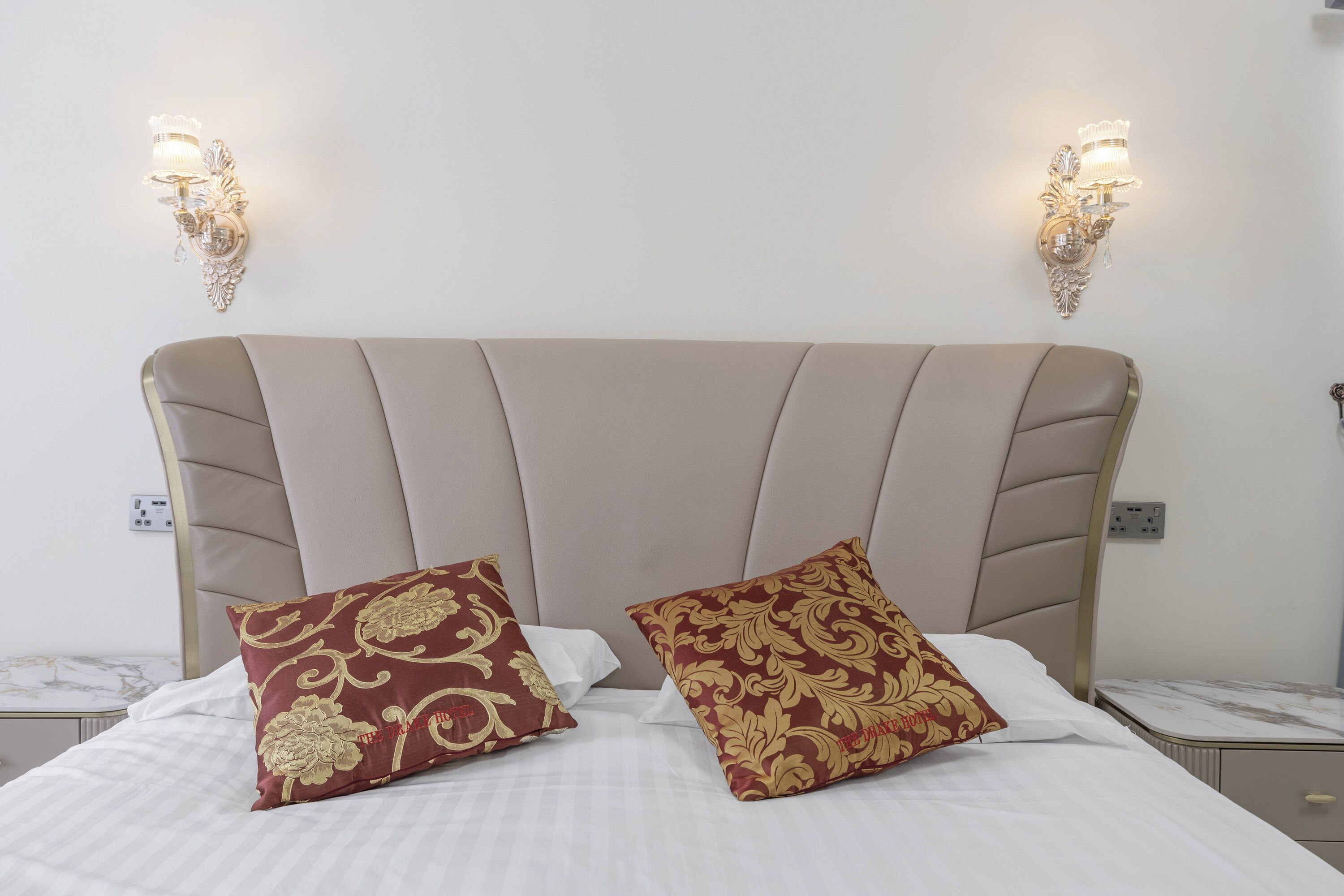 A bed with two decorative pillows, a headboard, and two wall-mounted light fixtures.